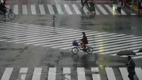People-Walking-And-Biking-At-Shibuya-Crossing-In-Tokyo,-Japan-Under-The-Rain---close-up,-slow-motion