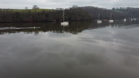 Two-rowers-row-on-a-still-flat-calm-stretch-of-river-with-yachts-moored-behind