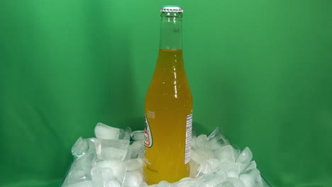 1-2-Kohlensäurehaltige-Mango-Getränkeflaschen,-Die-Sich-Um-360-Grad-Drehen,-Auf-Gestapeltem-Eis-Vor-Einem-Grünen-Bildschirm