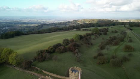 Dramatic-wide-aerial-pullback-reveal-shot-over-Broadway-tower,-an-English-landmark-stood-atop-Beacon-Hill-in-the-Cotswolds,-UK