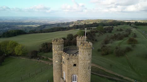 Aerial-view-rising-over-Broadway-tower,-an-English-landmark-stood-atop-Beacon-Hill-in-the-Cotswolds,-UK