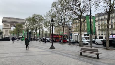Pedestrians-walking-along-the-Champs-Élysées-in-front-of-the-Arc-de-Triomphe,-one-of-the-major-landmarks-of-Paris,-France