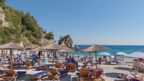 Pan-shot-of-a-picturesque-Greek-beach,-Parga-small-turquoise-water-beach-crowded-by-tourists