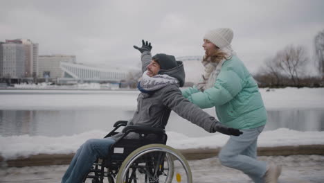 Happy-woman-running-with-her-disabled-friend-in-wheelchair-and-having-fun-together-in-the-city-in-winter
