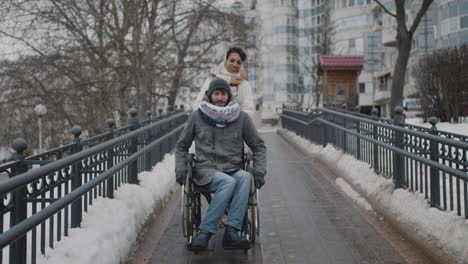 Vorderansicht-Einer-Muslimischen-Frau,-Die-Ihren-Behinderten-Freund-Im-Rollstuhl-Im-Winter-Auf-Einem-Spaziergang-In-Der-Stadt-Mitnimmt