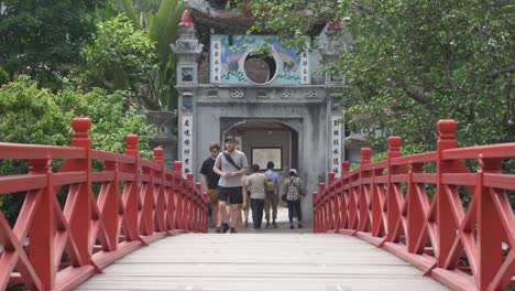 Walking-over-famous-red-Thê-Húc-Bridge-in-the-Old-Quarter-with-tourists-sightseeing-in-Hanoi,-Vietnam