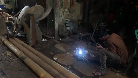 Panning-shot-of-a-man-welding-together-a-ship's-propellor-in-a-workshop-in-Sylhet