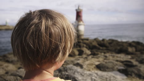 Young-boy-looking-at-a-lighthouse-at-the-beach