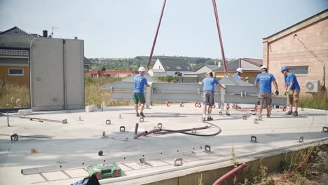 Construction-workers-installing-metal-beam-on-concrete-building-pad