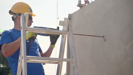 Construction-worker-on-stepladder-drilling-into-concrete-wall