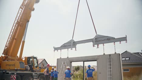 Construction-workers-installing-metal-traverse-on-wall-from-crane