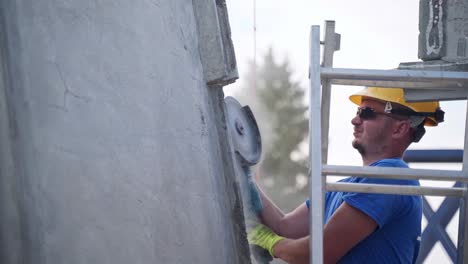 Construction-worker-in-sunglasses-grinding-concrete-wall-on-stepladder