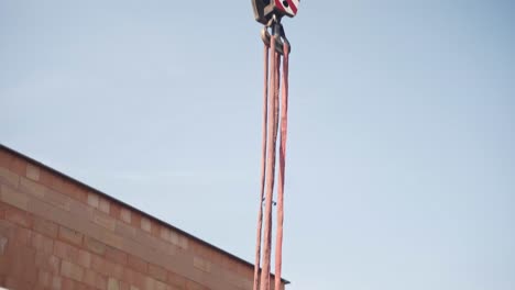 Construction-worker-securing-metal-beam-to-crane-cables-and-hook