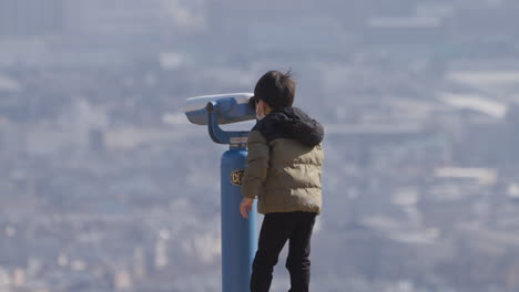 5-Jahre-Alter-Süßer-Junger-Asiatischer-Junge-In-Winterkleidung,-Der-Durch-Ein-Beobachtungsfernglas-Den-Blick-Auf-Die-Skyline-Der-Stadt-Kyoto-Genießt