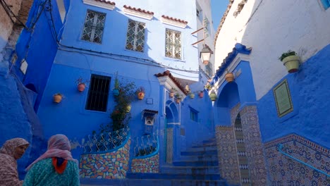 Moroccan-ladies-in-Typical-Blue-colored-Alleyway-staircase-in-Chefchaouen-old-town,-Morocco,-Tilt-down-shot