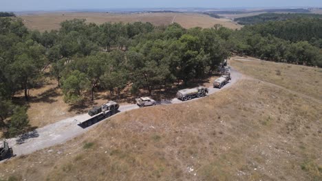 Israel-Army-infantry-squad-soldiers-on-vehicle-driving-through-green-field-at-training-ground-country-road,-Aerial-Tracking-shot
