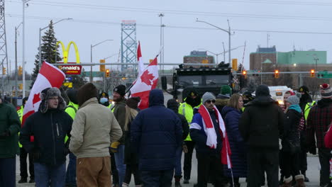 Static-shot-of-demonstrators-with-the-freedom-convoy-waving-Canadian-flags-protesting-against-the-COVID-vaccine-mandate-and-passport-with-the-Ambassador-bridge-and-police-in-the-background