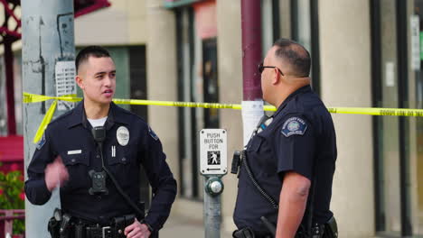 Two-Police-Officers-Stand-Guard-Outside-a-Crime-Scene-with-Caution-Tape-in-the-Background