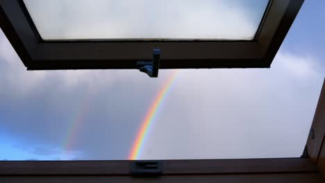 Look-through-window-in-the-attic-on-the-sky-with-few-clouds-and-rainbow
