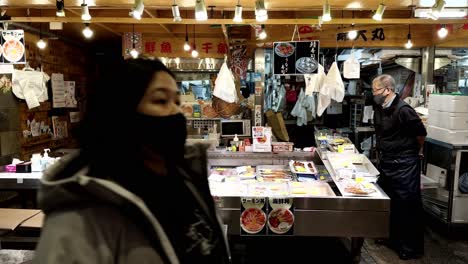 Pedestrians-strolling-past-local-seller,-indoor-market,-Kyoto,-Japan