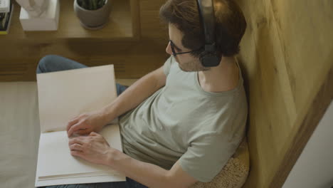 Top-view-of-caucasian-young-man-with-headphones-touching-a-book