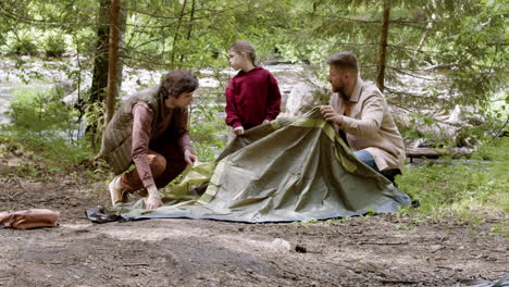 Young-family-setting-up-tent-near-the-river