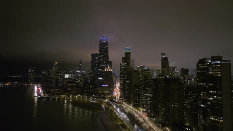 Illuminated-skyscrapers-and-traffic-in-Streeterville,-foggy-evening-Chicago,-US---pull-back,-drone-shot