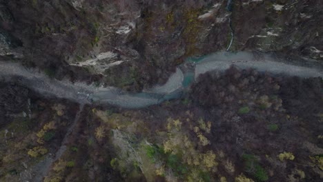 Relaxing-top-down-aerial-drone-sideways-shot-of-river-flowing-in-moody-winter-landscape-in-Switzerland-over-old-bridge
