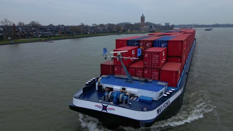 Luftorbitbewegung,-Schuss-Vom-Bug-Des-Binnenfrachters-Belicha,-Der-Intermodale-Container-Transportiert-Und-Entlang-Der-Oude-Maas-Durch-Dordrecht-Fährt
