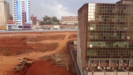 Construction-site-by-glossy-building-with-glass-exterior,-Yaoundé,-Cameroon,-pan-aerial-shot