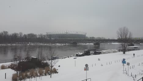 Drone-video-of-warsaw-national-stadium-while-train-passing-by-on-a-bridge-on-a-snowy-day-above-Vistula-river-2