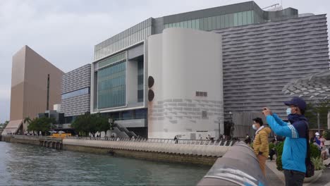 Museum-Of-Art-of-Hong-Kong-in-Tsim-Sha-Tsui,-the-modern-building-and-a-Chinese-person-with-a-mask-taking-photos