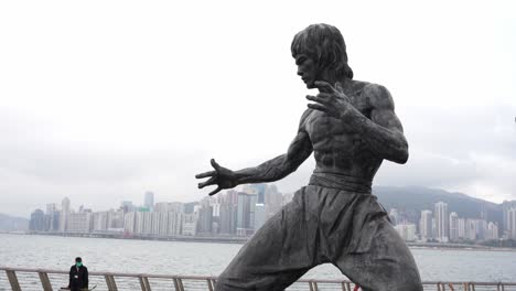 8.-Februar-–-Bruce-Lee-Statue-Auf-Hongkongs-Star-Walk-In-Tsim-Sha-Tsui-Mit-Der-Skyline-Von-Hongkong-Im-Hintergrund-An-Einem-Bewölkten-Tag