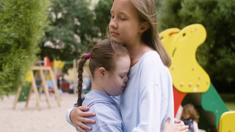 Close-up-view-of-a-little-girl-with-down-syndrome-hugging-another-girl-in-the-park-on-a-windy-day