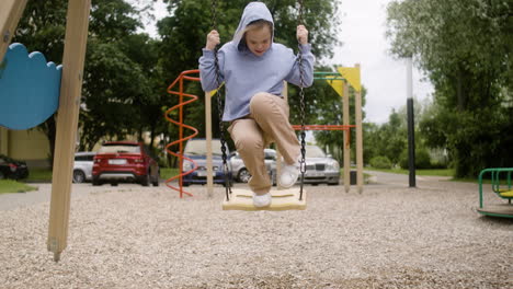 Little-girl-with-down-syndrome-wearing-hoodie-swinging-on-a-swing-in-the-park-on-a-windy-day