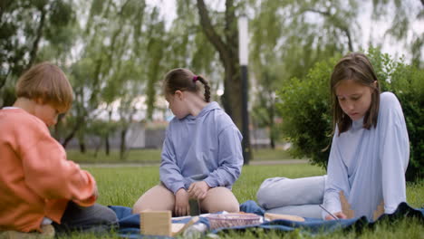 Little-girl-with-down-syndrome-doing-crafts-sitting-in-the-park-with-her-friends.-She-throws-a-piece-of-wood-back