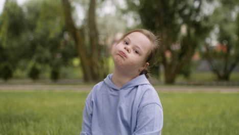 Little-girl-with-down-syndrome-smiling-at-camera-sitting-on-the-grass-in-the-park