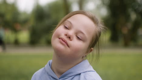 Close-up-view-of-a-little-girl-with-down-syndrome-looking-at-camera-sitting-on-the-grass-in-the-park