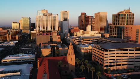 Wide-aerial-view-of-the-sun-setting-over-downtown-Phoenix,-Arizona-with-a-church-steeple-prominently-featured