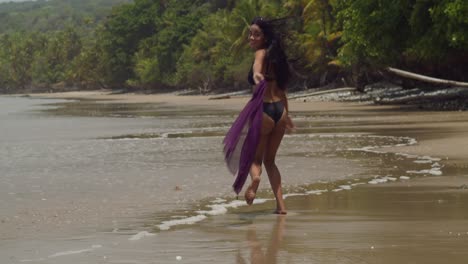 Eine-Sexy-Frau-In-Einem-Schwarzen-Bikini-Läuft-Am-Strand-Und-Vergnügt-Sich-Mit-Meereswellen-Im-Hintergrund