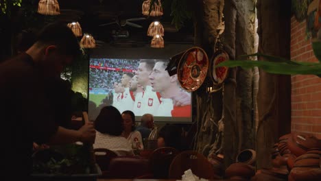 A-sports-bar-showing-a-football-match-on-a-big-screen,-with-Robert-Lewandowski-singing-the-Polish-national-anthem