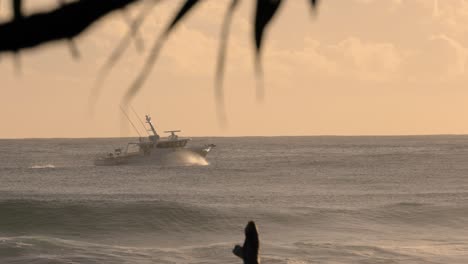 Boat-passing-surfers-at-sunrise-at-Burleigh-Heads-on-the-Gold-Coast,-Queensland,-Australia