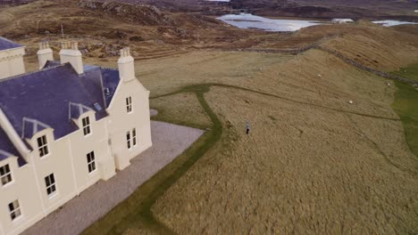 Drone-shot-of-fiddler-playing-his-violin-by-a-country-estate-on-the-Isle-of-Lewis,-Outer-Hebrides-of-Scotland,-United-Kingdom