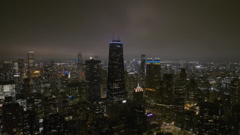 Aerial-view-of-the-John-Hancock-tower,-hazy-night-in-Chicago,-USA---pull-back,-drone-shot