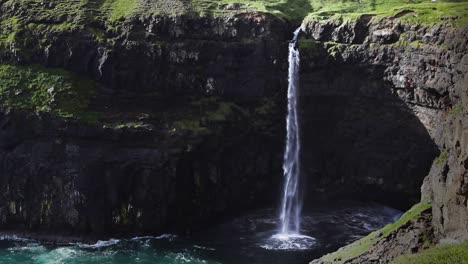 Shot-of-Múlafossur-waterfall-with-birds-flying-and-crashing-waves-against-coastline-on-Vagar-Island,-Faroe-Island
