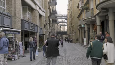 Pan-down-to-London-Shad-Thames-cobblestone-street-with-people-and-bicycles-in-slow-motion