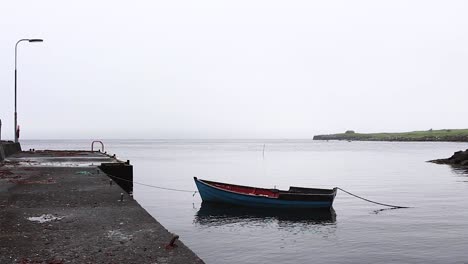 Wooden-boat-tied-to-pier-on-a-calm-ocean-foggy-day-in-the-Faroe-Islands