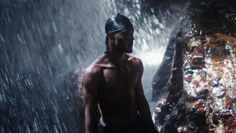 Young-black-man-stands-under-waterfall-while-travelling-and-exploring