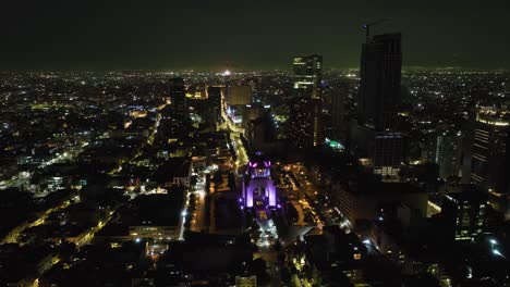 Aerial-view-circling-around-the-illuminated-Revolution-Monument,-night-in-Mexico-city
