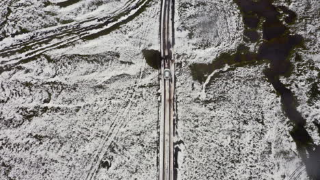 Luftaufnahme:-Von-Oben-Nach-Unten,-Verfolgungsaufnahme-Eines-Autos,-Das-Auf-Einer-Teilweise-Schneebedeckten-Bergstraße-In-Island-Fährt